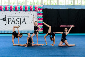 Grupowy układ gimnastyczny zawierający różne pozycje i figury wykonany przez zawodniczki szkoły Gimnastyki Artystycznej Pasja